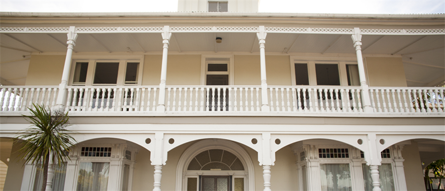 A white veranda with lots of detail and ornate pillars in front of a two-storey house.