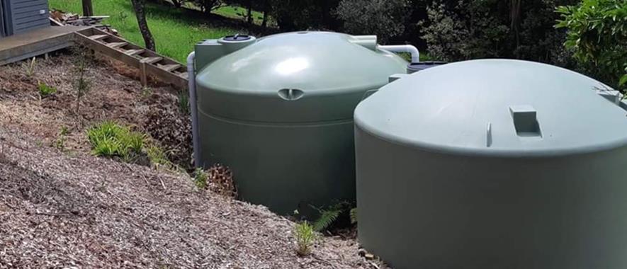 Two large water tanks sitting side by side on a slope.