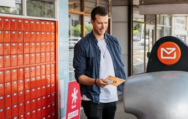 Photograph of a man putting an envelope in a NZ Post mail box.