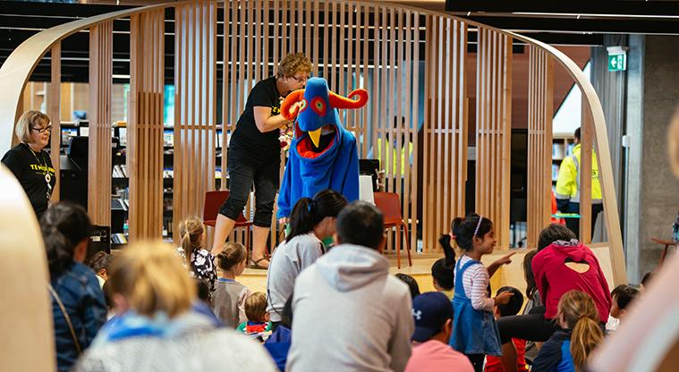 Children and parents watch the stage where someone is dressed as a blue creature with long red horns.