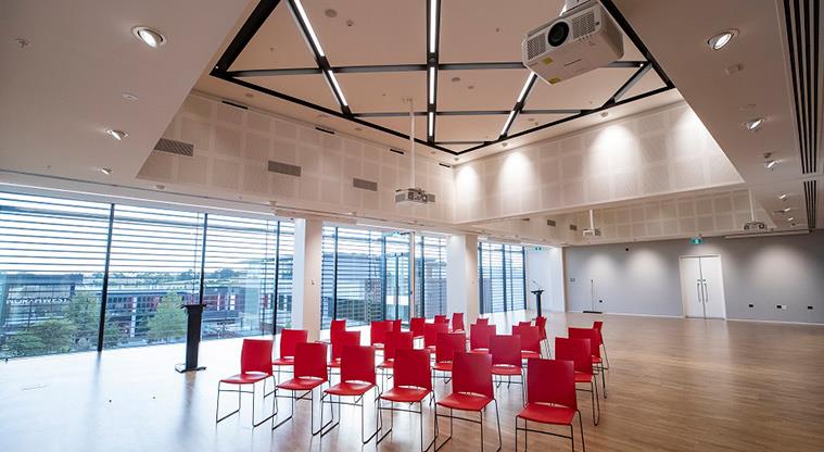 Rows of empty red seats in a large, brightly lit auditorium.
