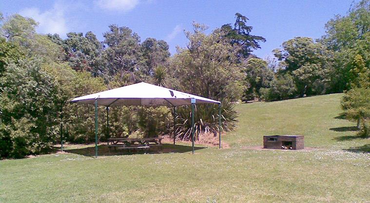 Awhitu Regional Park - Bookable site with shelter over picnic tables, a barbecue, open space and trees.
