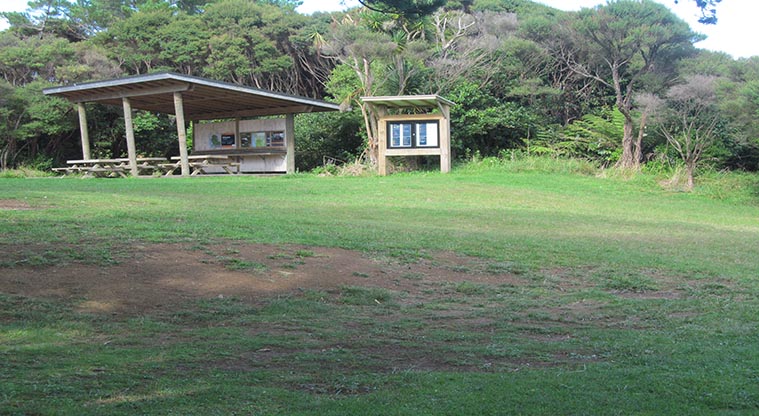 Craw Campground - Grass area with covered seating area and noticeboard in the background.