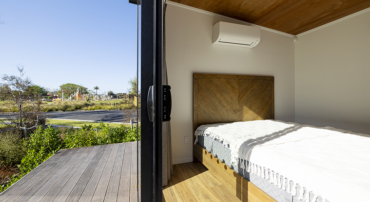 Te Kopua tiny home - The bedroom and section of the deck with the road and trees in the background.
