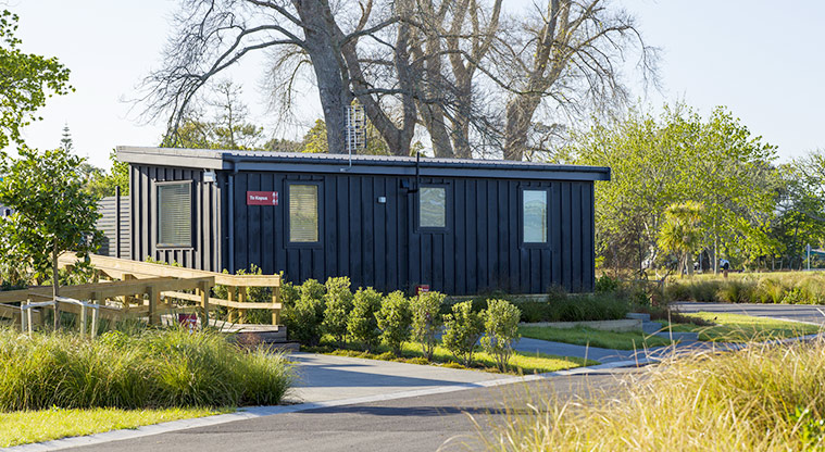 Te Kopua tiny home - View of Te Kopua from the road with trees in the background.
