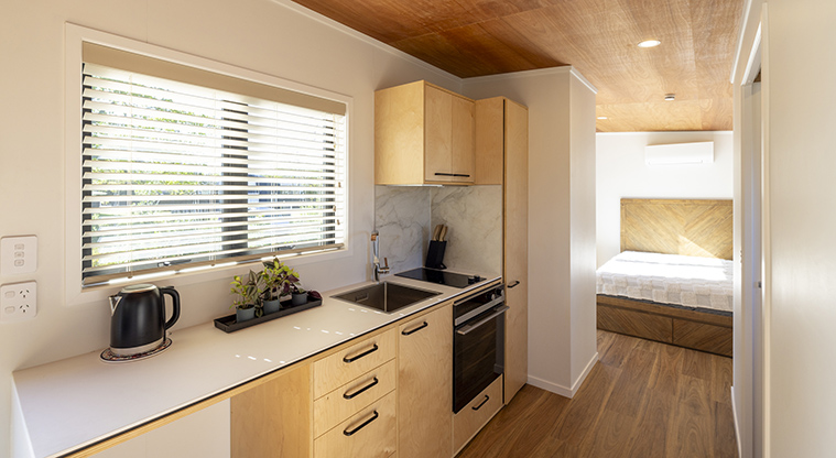 Te Kopua tiny home - Kitchen area and facilities with the bedroom in the background.