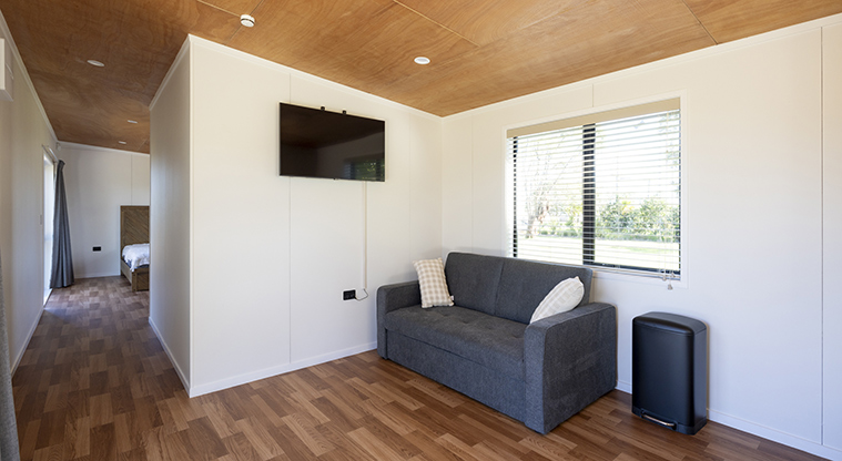 Te Tino tiny home - Lounge area with a television on the wall and the hallway and bedroom in the background.