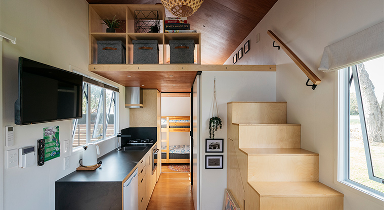 Mahana tiny home - Kitchen with the bunk bedroom in the background and stairs up to the mezzanine (upper level) bedroom.