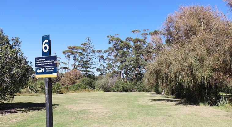 Long Bay Regional Park - Bookable site six sign with open grassed space and trees in the background.