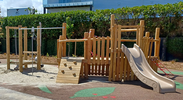 86 Harvest Avenue - Low wooden structure with a climbing wall, raised platform, low slide and a sand play area.