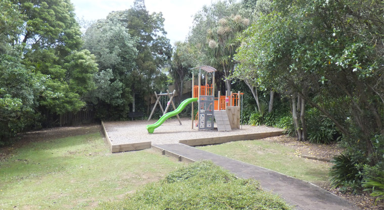 Aitken Reserve - Open grassed space with the path leading into the play area, with trees in the background. Photo credit: J Grigg.