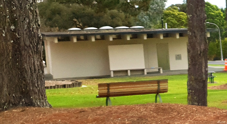 Blockhouse Bay Recreation Reserve - Seat under the tree and toilet block in the background.
