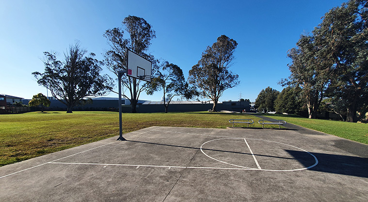 Bob Hill Reserve - Basketball half-court and hoop, with open grassed space, seats and trees in the background.