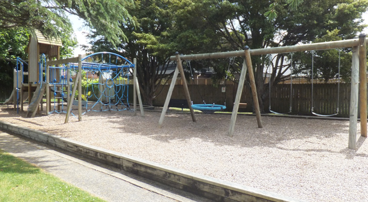 Braemar Reserve - Set of two swings, a basket swing, and the rest of the playground and trees in the background. Photo credit: J Grigg.