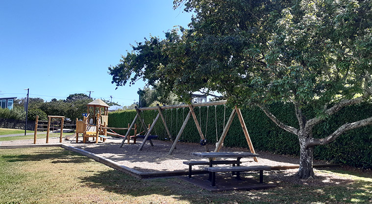 Centennial Park - Playground with climbing equipment and slide, a swing set, and picnic table in the foreground.