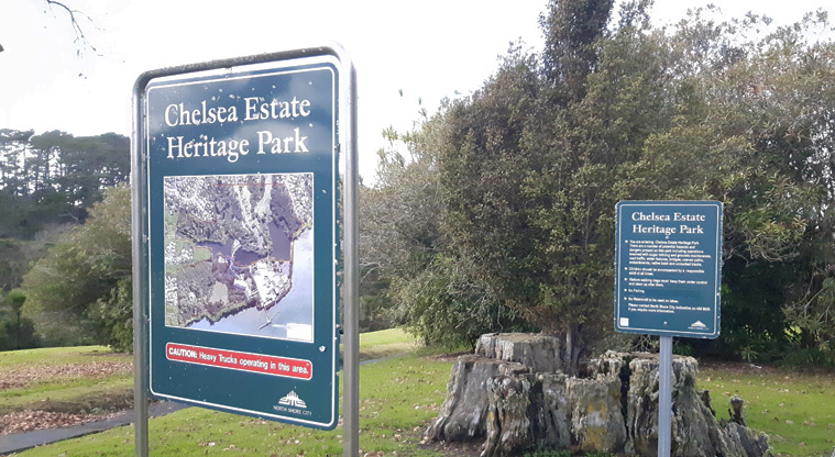 Chelsea Estate Heritage Park - Signage at the entrance to the park with an old tree stump and other trees in the background.