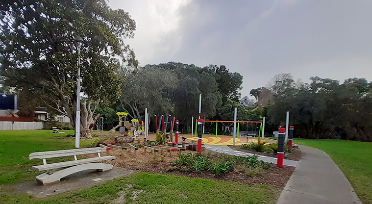 Cockle Bay Reserve - A bench seat with the playground, open space and trees in the background.