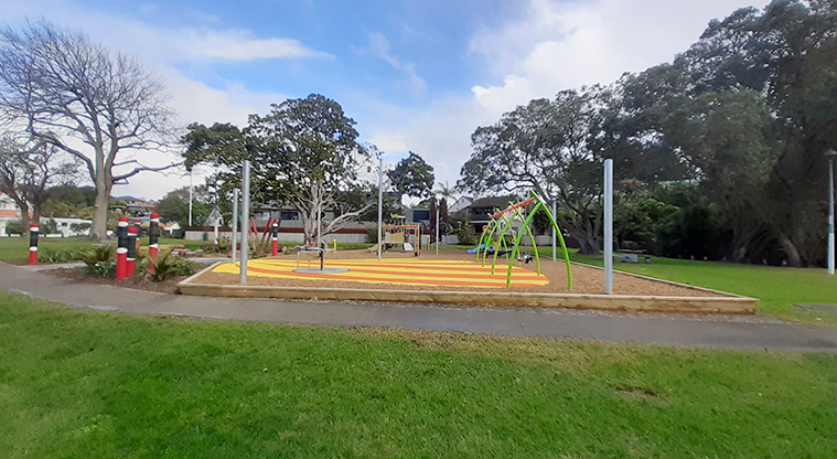Cockle Bay Reserve - Open grassed space and a section of footpath with the whole playground and large trees in the background.