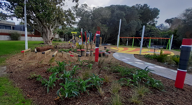Cockle Bay Reserve - Nature area with plants, a large fallen log, and balance beams and stumps.
