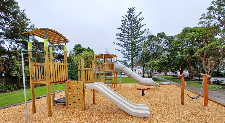 Collins Park - Two play modules with slides, a low sling swing and small rocker toy with trees and open space in the background.
