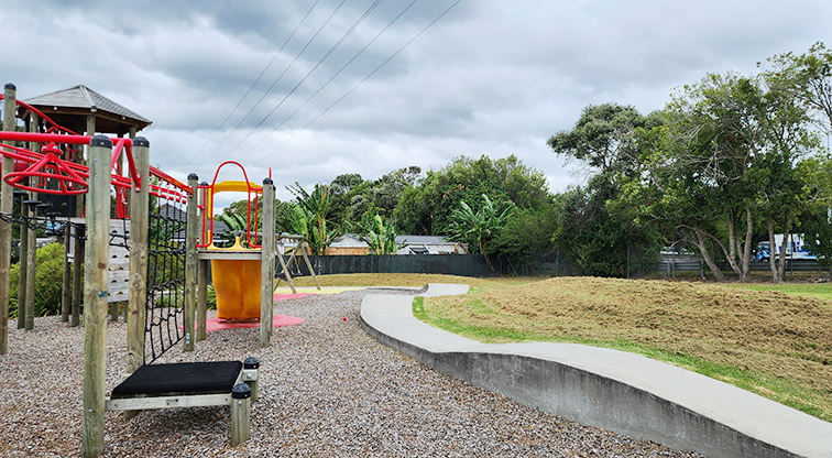Toetoe-roa / Cooper Park - Part of the play module with a bike path running along the right-hand side, open grassed space and trees.
