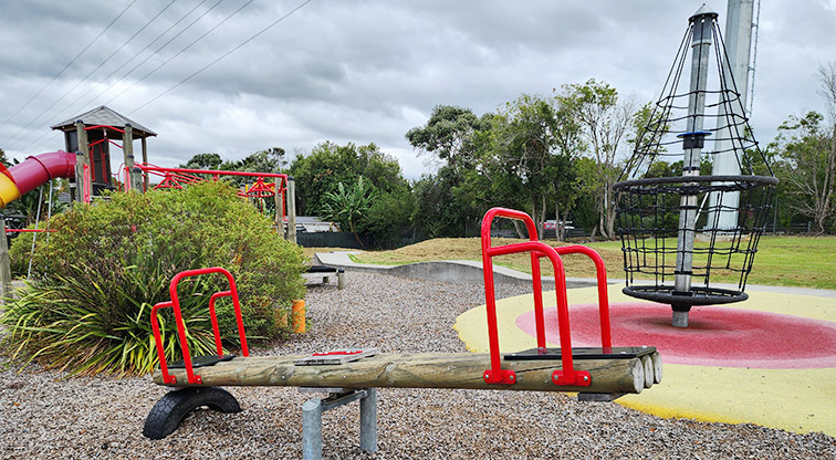 Toetoe-roa / Cooper Park - Seesaw with the net climbing frame, part of the play module, and open space in the background.
