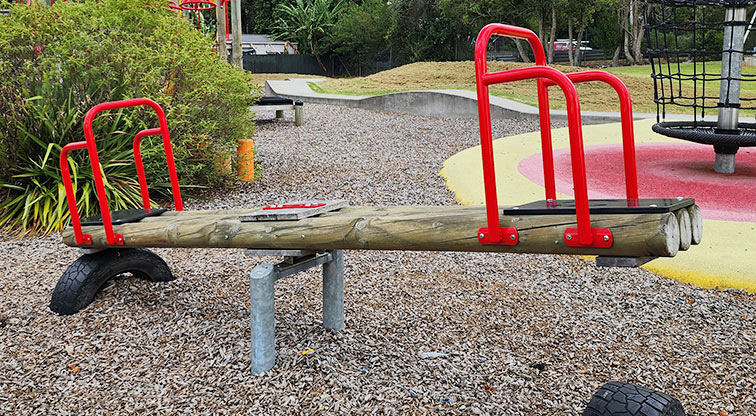 Toetoe-roa / Cooper Park - Seesaw with the net climbing frame and open space in the background.