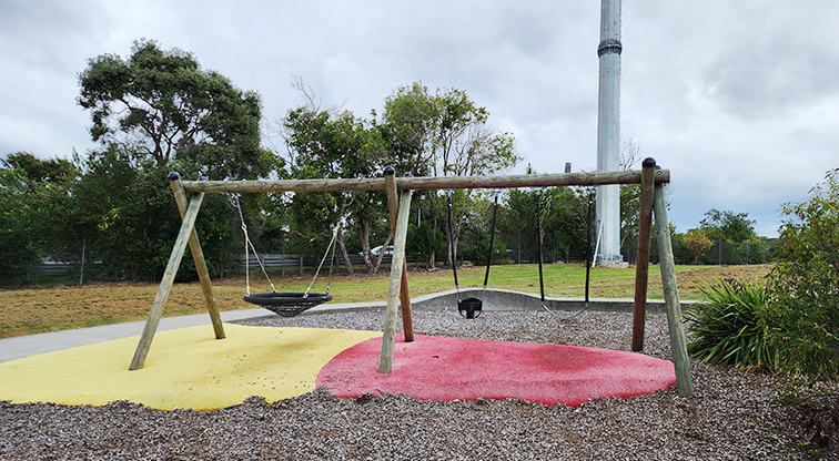 Toetoe-roa / Cooper Park - Swing set with a basket swing, bucket swing and belt swing and open grassed space in the background.