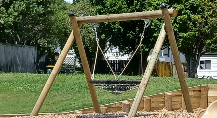 Cranston Street Reserve - Stand-alone basket swing with grassed space and trees in the background.
