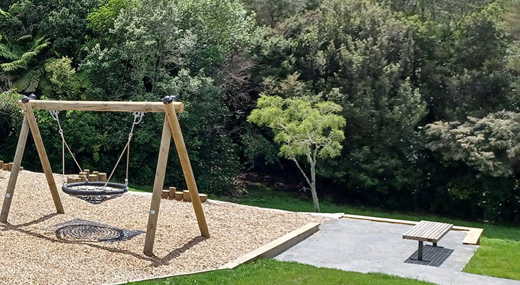 Cranston Street Reserve - The basket swing with a flat concrete area and seat on the right. and bush in the background.