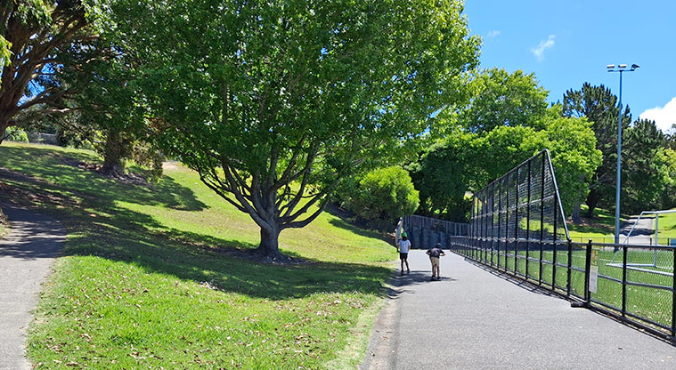 Tahurangi / Crum Park - Two children on scooters on one of the paths with trees on the left and the fenced sports fields on the right. Photo credit: T Hodder.