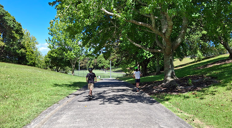 Tahurangi / Crum Park - Two children on scooters on one of the paths with trees on both sides and sports fields in the background. Photo credit: T Hodder.