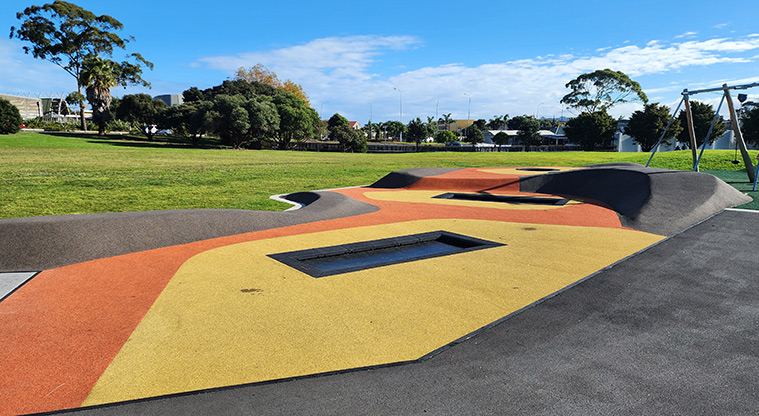 David Lange Park - Brightly coloured soft-fall surface with in-ground trampolines, and open grassed space and trees in the background.
