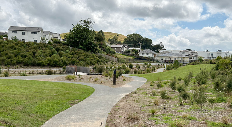Freeland Reserve - A section of the path with grassed and planted areas, and a bridge in the background. Photo credit: S Hulse.