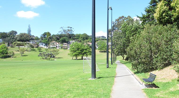 Glover Park - Section of the sports field with a path and seat along the right hand edge.
