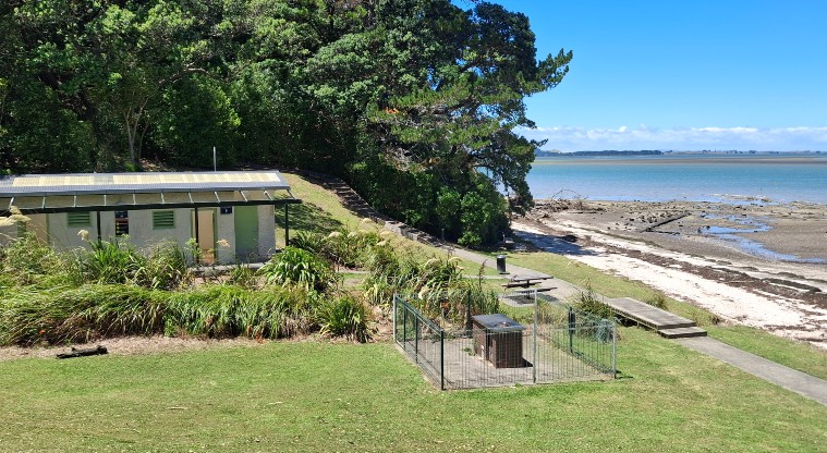 Tauihu / Green Bay Beach - Beach with a barbecue, toilets and picnic table in the foreground. Photo credit: T Hodder.