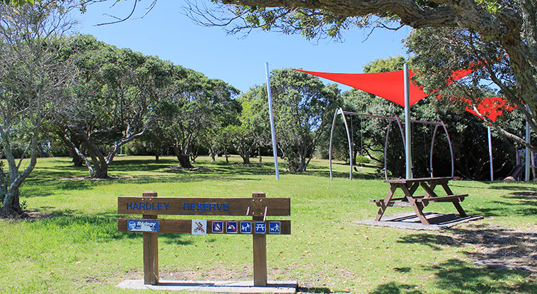 Hardley Reserve - Sign at the entrance to the reserve, with a picnic table, playground and trees in the background. Photo credit: M Loubser.
