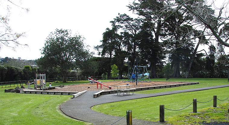 Henderson Valley Park – Open grassed area with the playground, a picnic table and trees. Photo credit: Tracey Hodder.