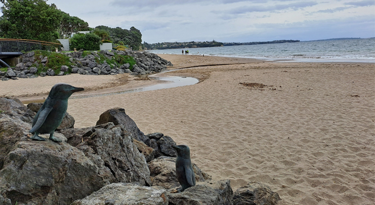 Poa Taniwha / Huntly Road Reserve – A view of the beach overlooked by bronze statues of little blue penguins / kororā. Photo credit: M Woodside.