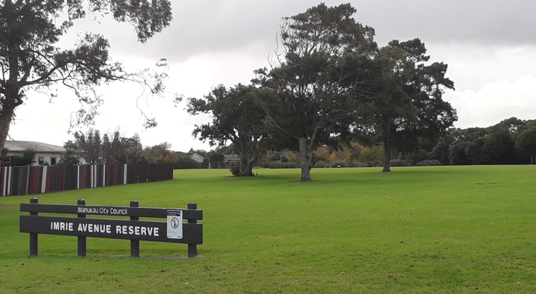 Imrie Park - Sign at the entrance to the park with grassed open space and large trees in the background.