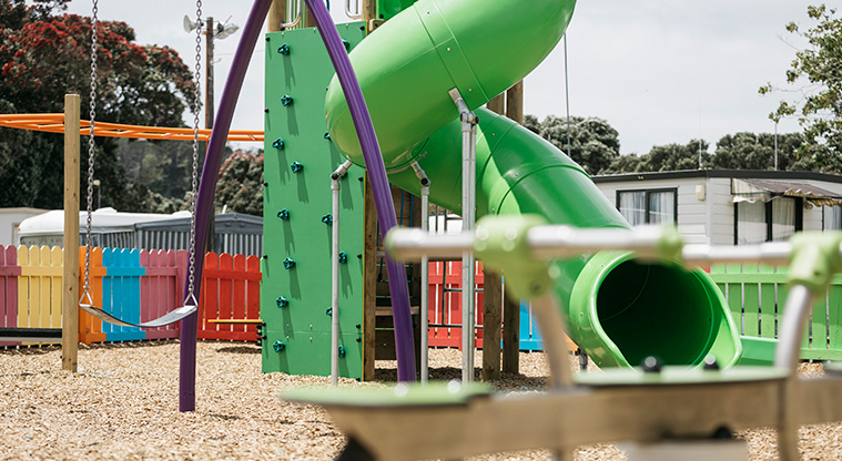 Martins Bay Holiday Park - Section of the high green slide with a swing and colourful picket fence in the background.