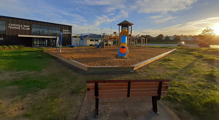 Meadowlland Park - Colourful playground with a large slide, set of three swings, and a seat in the foreground.