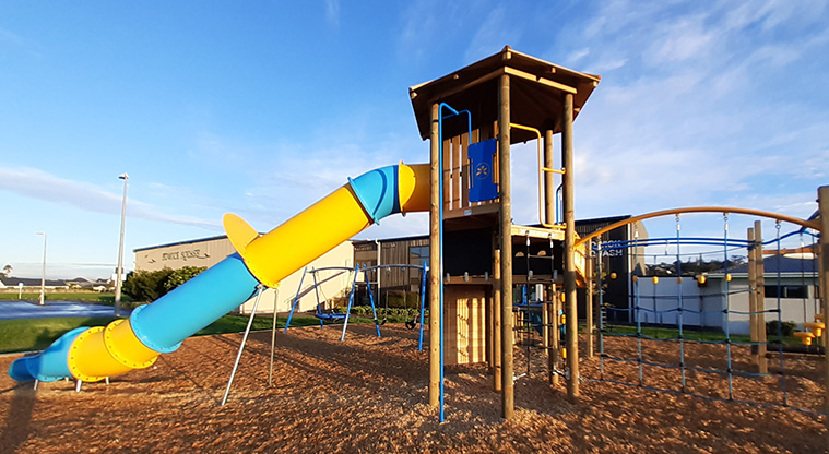 Meadowland Park - Side view of the high slide running down from the tower, climbing nets, and the swings in the background.
