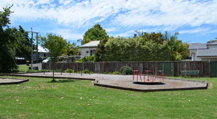 Melrose Reserve - Open grassed area with part of the playground with roundabout and swings in the background.