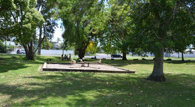 Melrose Reserve - Open grassed area with trees, and a section of the playground with a seesaw.