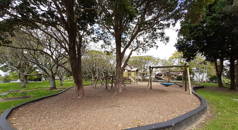Melville Park - Wooden playground under the trees with climbing equipment, swings and slides.