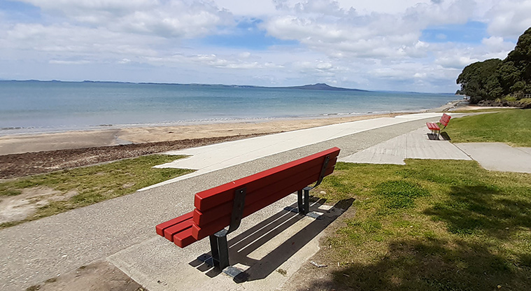 Murrays Bay Beach Reserve - Bright red bench seat by the footpath and looking out to Rangitoto Island.