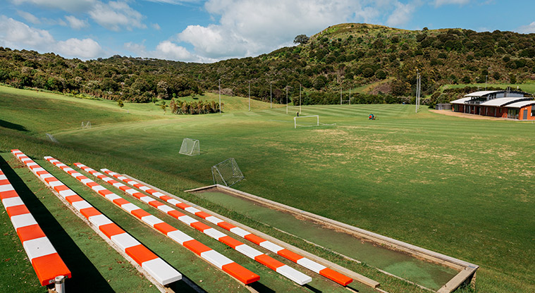 Onetangi Sports Park - Red and white striped bench seating up the hill with sports fields and the pavilion in the background.