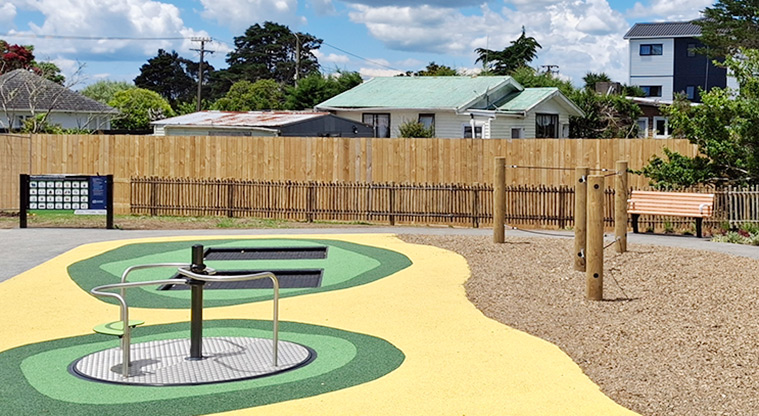 Rānui Domain - Inclusive seated spinner with the in-ground trampolines and communication board in the background.