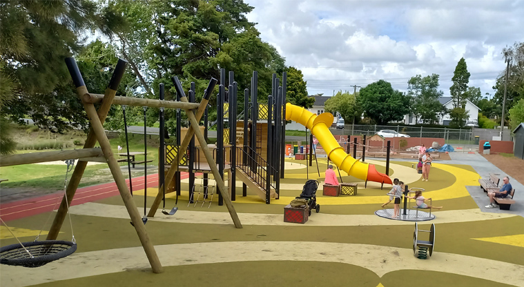 Riverhead War Memorial Park - View of a vibrant playground with swings, slides, a merry-go-round and more.